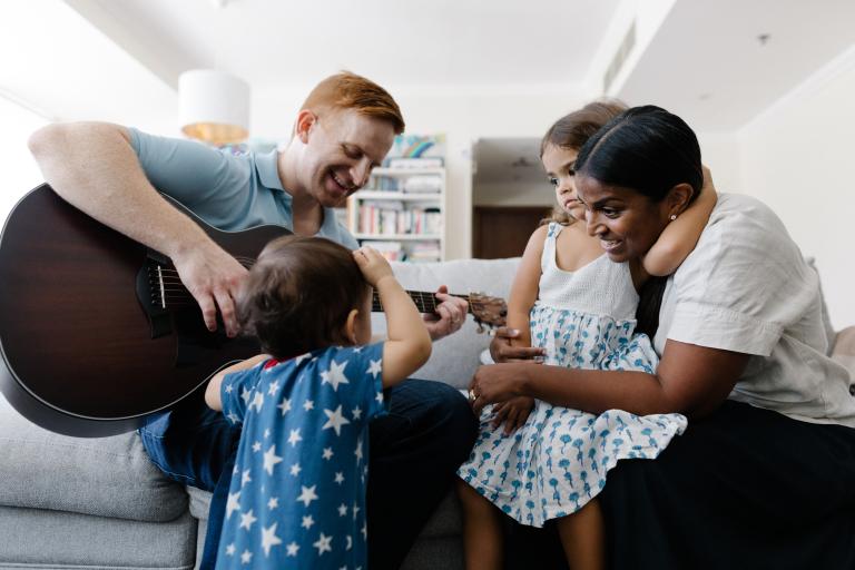Man playing guitar while lady and 2 young children watch