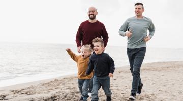 Same sex couple foster carers running with children on the beach