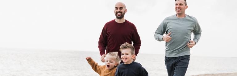 Same sex couple foster carers running with children on the beach